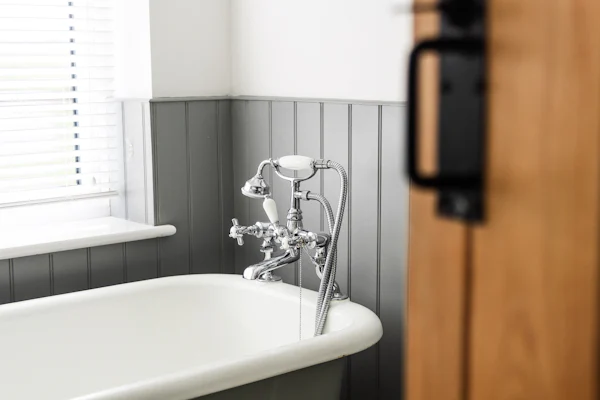 Clawfoot tub against gray beadboard beside a sunny window