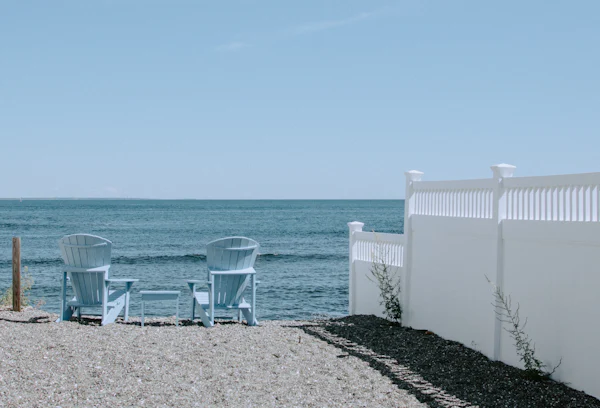 Two white Adirondack chairs on the sand facing the ocean