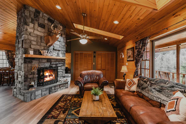 Knotty pine living room with a stone fireplace, leather sofa, and wood beams